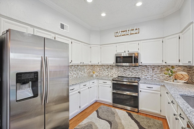 kitchen with white cabinetry, stainless steel appliances, light stone counters, and backsplash