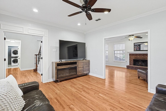 living room with crown molding, stacked washer and dryer, a fireplace, and light hardwood / wood-style floors