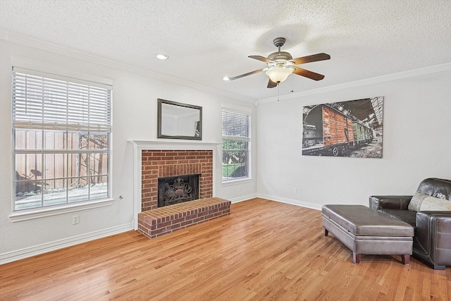 living area featuring a brick fireplace, ornamental molding, ceiling fan, and light wood-type flooring