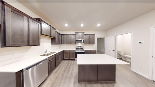 kitchen with dark brown cabinetry, appliances with stainless steel finishes, a kitchen island, sink, and light wood-type flooring