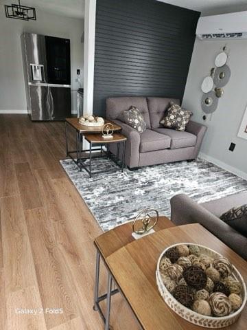 living room with an AC wall unit, wood finished floors, and baseboards