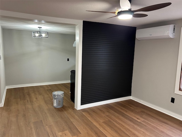 spare room with a wall mounted AC, ceiling fan with notable chandelier, and wood-type flooring