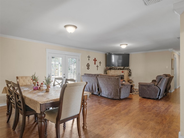 dining space featuring hardwood / wood-style floors, crown molding, french doors, and a fireplace