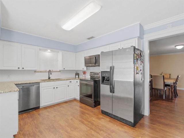 kitchen with white cabinets, appliances with stainless steel finishes, sink, ornamental molding, and light wood-type flooring