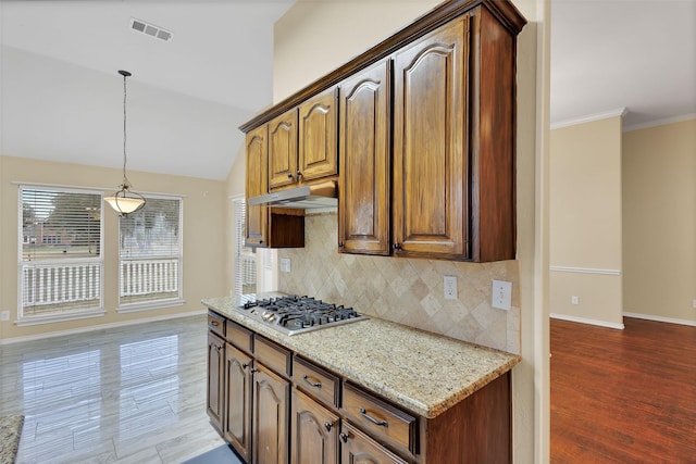 kitchen with hanging light fixtures, backsplash, ornamental molding, light stone countertops, and stainless steel gas stovetop