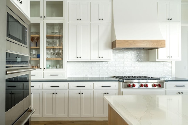 kitchen with appliances with stainless steel finishes, white cabinets, custom range hood, and tasteful backsplash