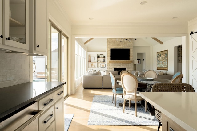 interior space featuring crown molding, vaulted ceiling with beams, a fireplace, light wood finished floors, and a barn door