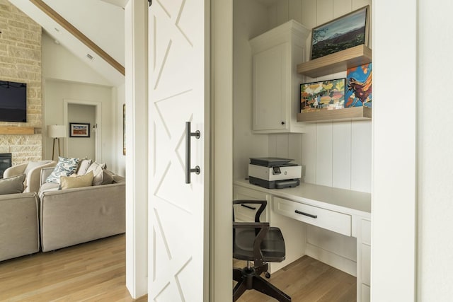 office area featuring vaulted ceiling, a stone fireplace, built in desk, and light wood-type flooring