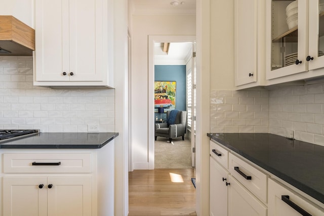 kitchen with dark countertops, wood finished floors, glass insert cabinets, and crown molding