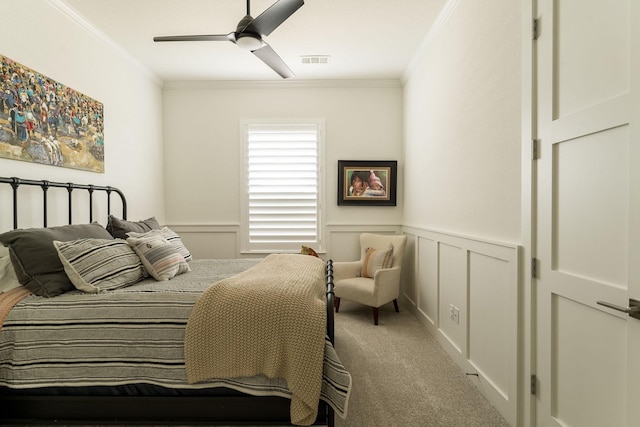 bedroom with carpet flooring, ceiling fan, a wainscoted wall, visible vents, and ornamental molding