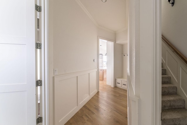 hall featuring light wood-type flooring, a wainscoted wall, a decorative wall, and crown molding
