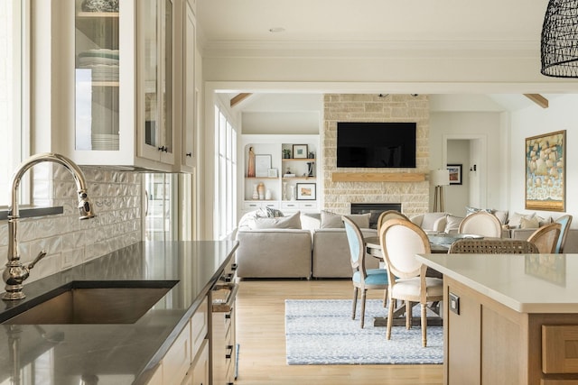 kitchen with light wood finished floors, a sink, crown molding, a fireplace, and glass insert cabinets
