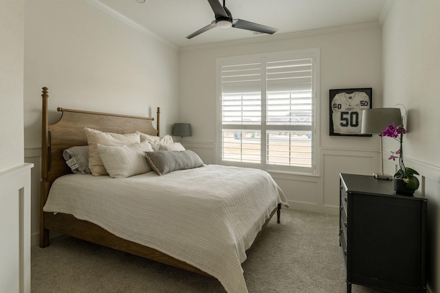 bedroom featuring a wainscoted wall, ornamental molding, a ceiling fan, and light colored carpet