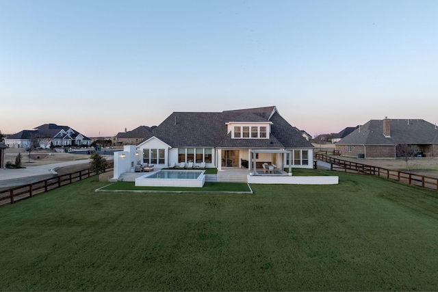 back house at dusk featuring a patio area and a yard