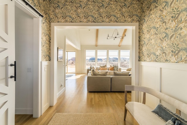 living room with a wainscoted wall, beamed ceiling, light wood-type flooring, and wallpapered walls