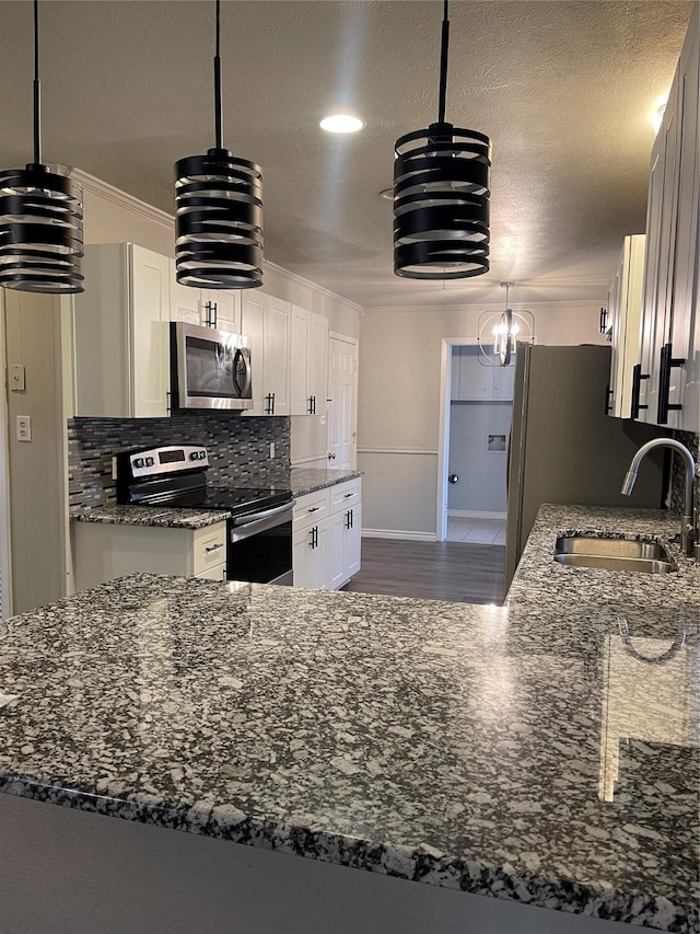 kitchen with appliances with stainless steel finishes, pendant lighting, white cabinets, and sink