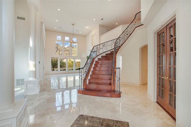 foyer entrance with ornate columns, a towering ceiling, and french doors