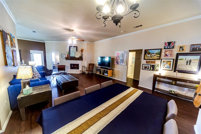 living room featuring ceiling fan with notable chandelier, dark wood-type flooring, a large fireplace, and ornamental molding