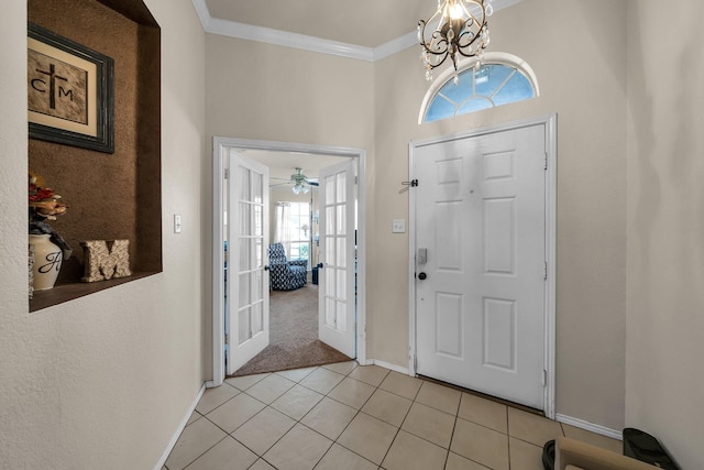 tiled entrance foyer featuring ornamental molding, ceiling fan with notable chandelier, and french doors