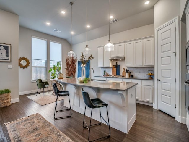 kitchen with decorative light fixtures, a kitchen bar, an island with sink, and white cabinetry