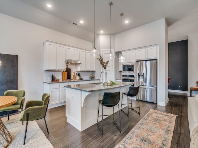 kitchen featuring appliances with stainless steel finishes, white cabinetry, hanging light fixtures, and a kitchen island with sink