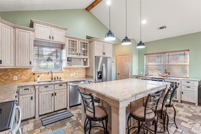 kitchen with appliances with stainless steel finishes, a kitchen island, decorative backsplash, sink, and beam ceiling