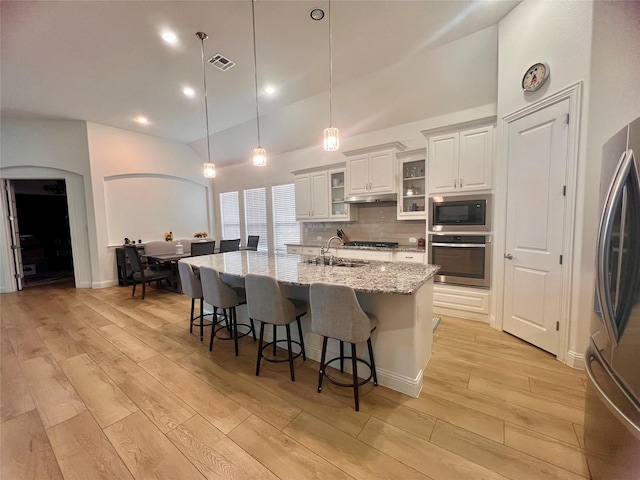 kitchen with white cabinetry, hanging light fixtures, a kitchen island with sink, light stone countertops, and stainless steel appliances