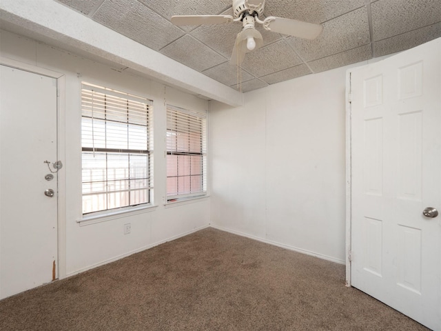 carpeted empty room featuring ceiling fan and a drop ceiling