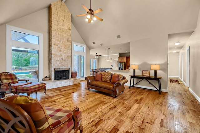 living room featuring light wood-type flooring, plenty of natural light, a stone fireplace, and high vaulted ceiling