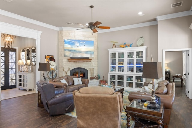 living room with dark wood-type flooring, ceiling fan, ornamental molding, and a stone fireplace