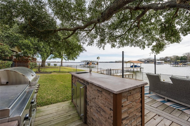 deck with grilling area, exterior bar, a lawn, and a water view