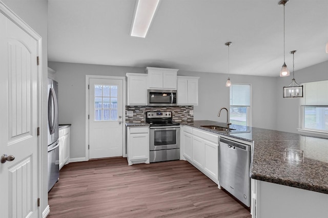 kitchen with white cabinetry, stainless steel appliances, dark stone counters, sink, and hanging light fixtures