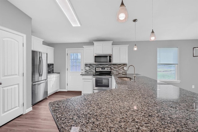 kitchen with tasteful backsplash, dark stone countertops, pendant lighting, sink, and appliances with stainless steel finishes