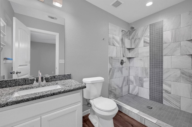 bathroom with hardwood / wood-style floors, tiled shower, vanity, and toilet