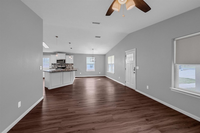 unfurnished living room featuring vaulted ceiling, ceiling fan, plenty of natural light, and dark hardwood / wood-style floors