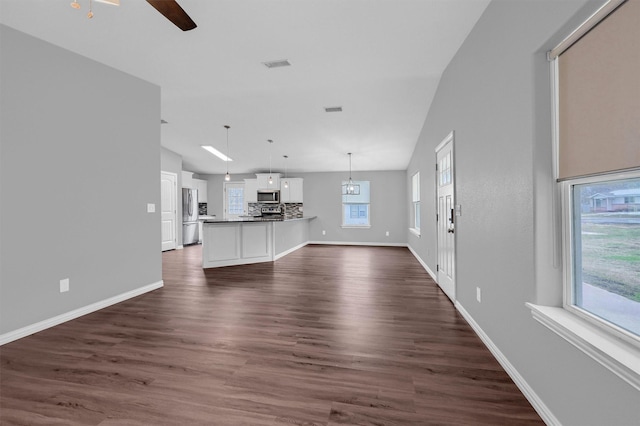 unfurnished living room with ceiling fan, a wealth of natural light, dark hardwood / wood-style flooring, and vaulted ceiling