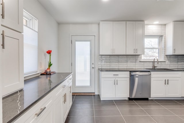 kitchen with dark stone countertops, stainless steel dishwasher, sink, dark tile patterned floors, and white cabinets