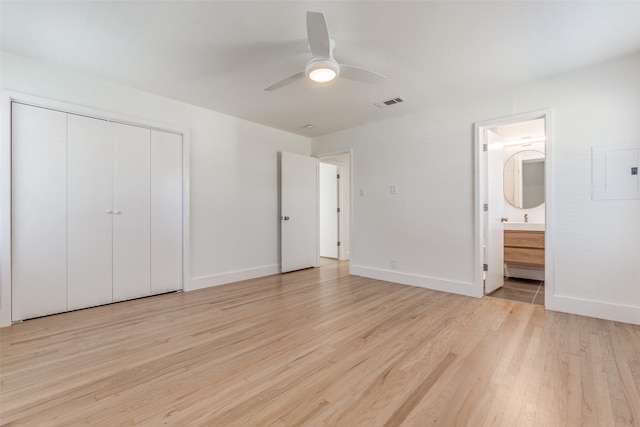 unfurnished bedroom with ceiling fan, electric panel, ensuite bath, light hardwood / wood-style flooring, and a closet