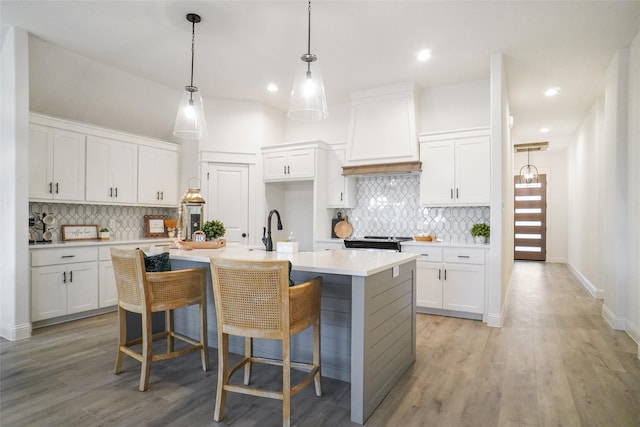 kitchen featuring white cabinets, a breakfast bar, an island with sink, and premium range hood