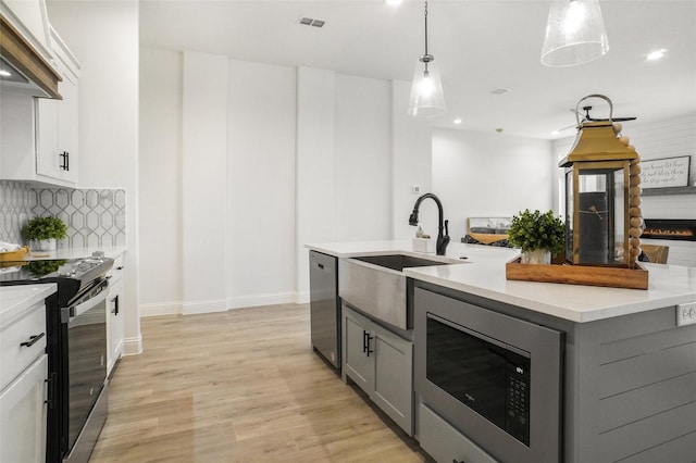 kitchen with white cabinets, black / electric stove, hanging light fixtures, a center island with sink, and built in microwave