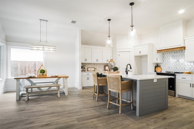 kitchen featuring white cabinets, stainless steel electric range oven, and an island with sink