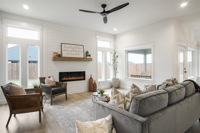 living room featuring ceiling fan, a large fireplace, and light hardwood / wood-style flooring