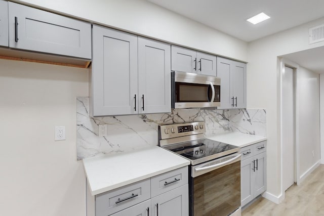 kitchen with tasteful backsplash, stainless steel appliances, light hardwood / wood-style floors, and gray cabinetry