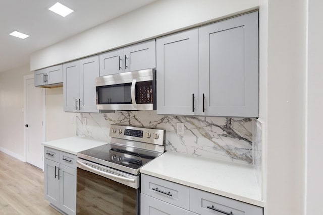 kitchen featuring gray cabinetry, decorative backsplash, light hardwood / wood-style flooring, and stainless steel appliances