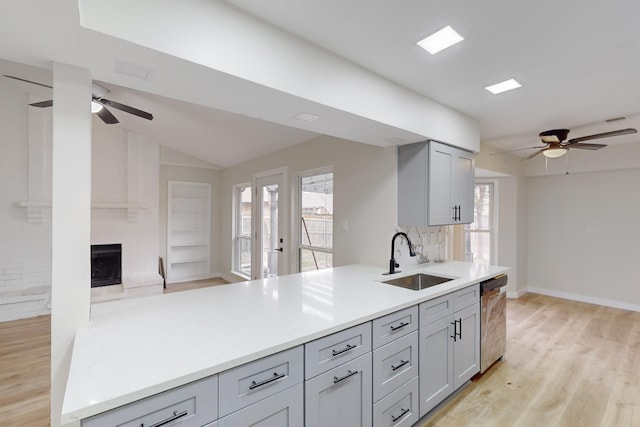 kitchen with sink, light hardwood / wood-style flooring, gray cabinets, a fireplace, and stainless steel dishwasher