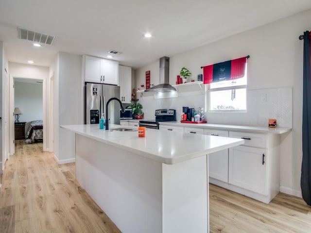 kitchen with a center island with sink, sink, stainless steel appliances, white cabinets, and wall chimney exhaust hood