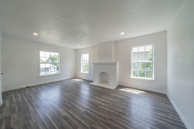 unfurnished living room with a textured ceiling, dark wood-type flooring, a wealth of natural light, and a fireplace