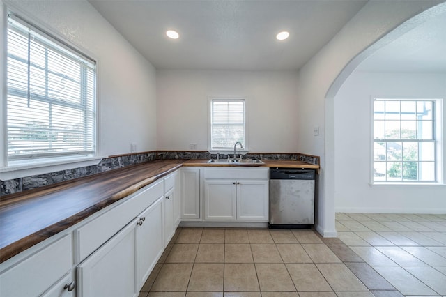 kitchen with dishwasher, wood counters, white cabinetry, sink, and light tile patterned floors