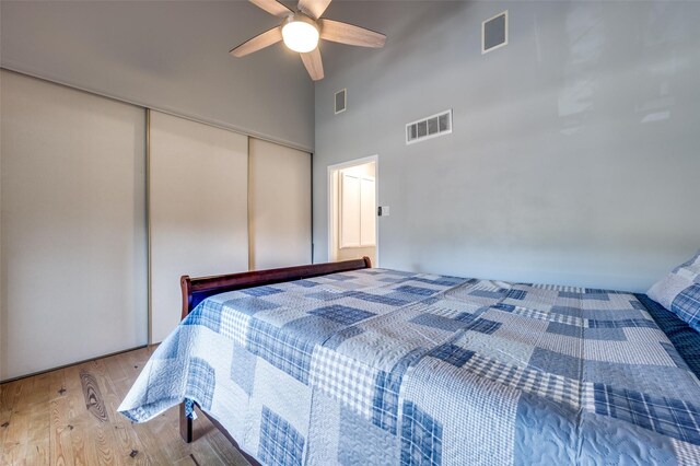 bedroom featuring ceiling fan, a closet, a towering ceiling, and light hardwood / wood-style flooring