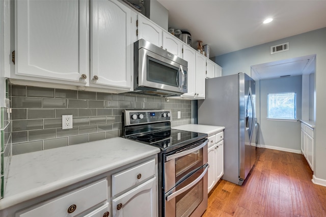 kitchen featuring white cabinets, appliances with stainless steel finishes, light hardwood / wood-style flooring, and tasteful backsplash